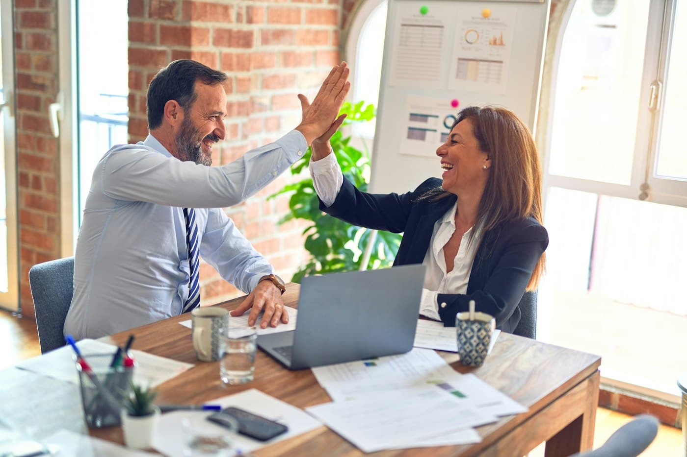 Two founders celebrating at a desk after closing the sale of their company