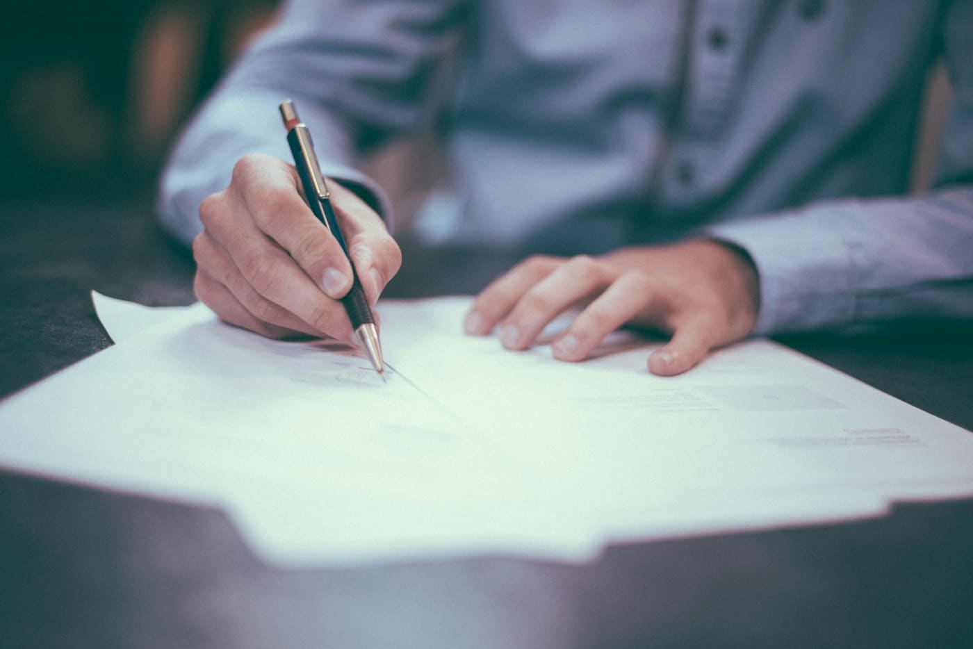 A hand signing a printed agreement with a fountain pen